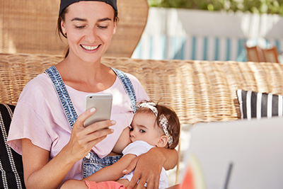 Young mother using smartphone while nursing infant